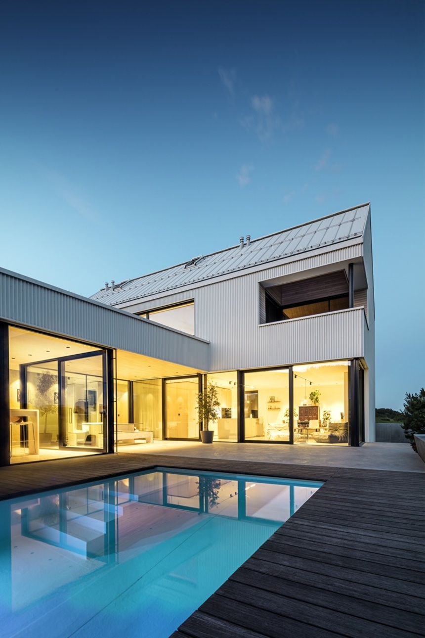 Večerní osvětlení domu s bílou hliníkovou fasádou a bazénem.